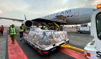 Avión de carga con medicamentos siendo descargado en un aeropuerto, con personal especializado manipulando cajas marcadas con símbolos médicos